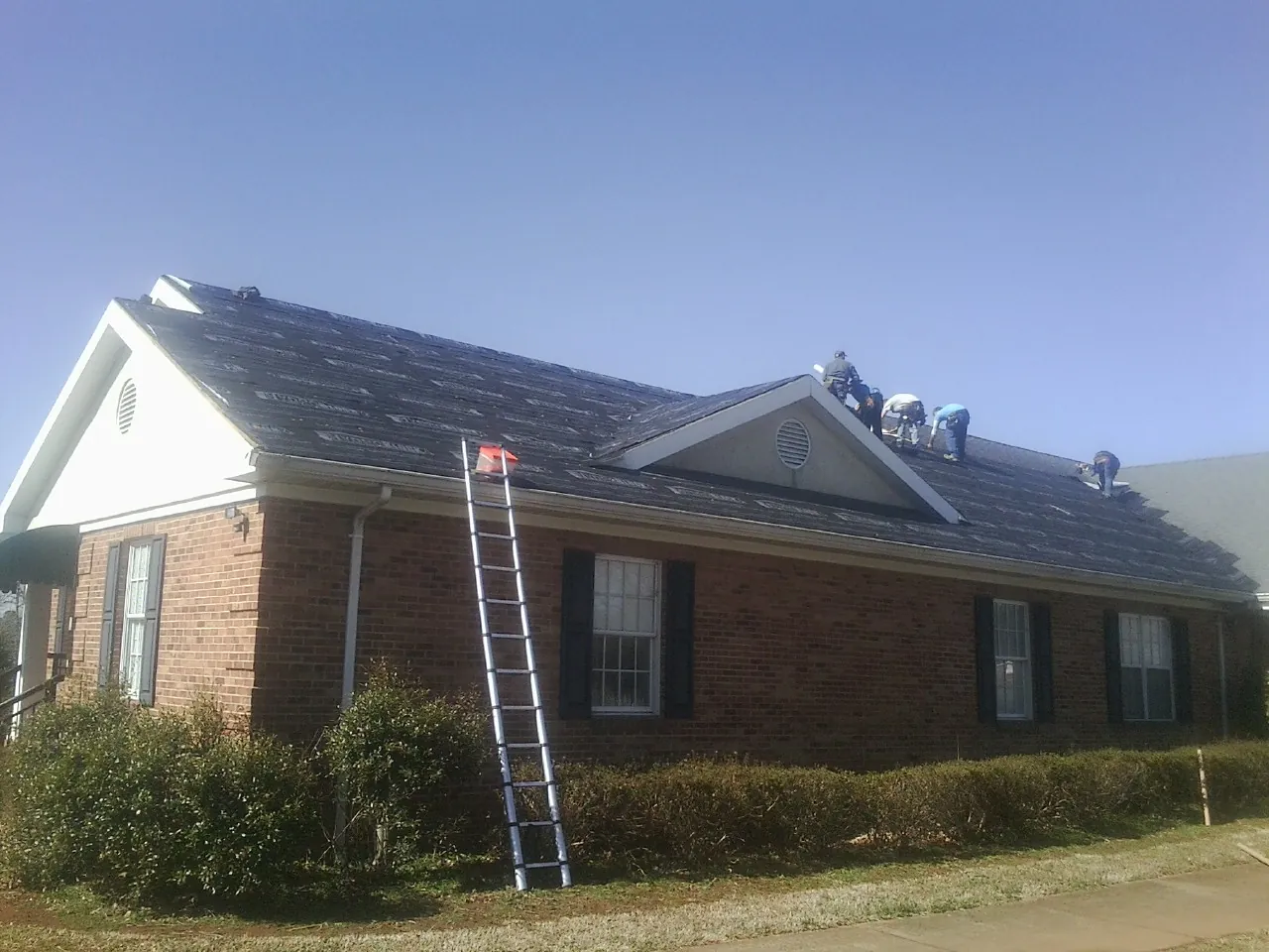 Crew tearing shingles off a brick ranch roof with a ladder set — Metal Roof Repair work by our crew in Circleville